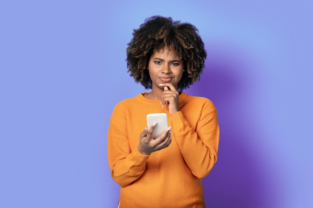 Смущенная молодая черная женщина со смартфоном в руке