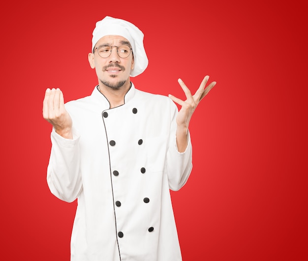 Confused young chef making an italian gesture of not understand