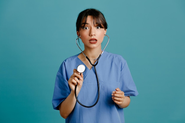 写真 青い背景で隔離の均一なフィス聴診器を身に着けている混乱した若い女性医師