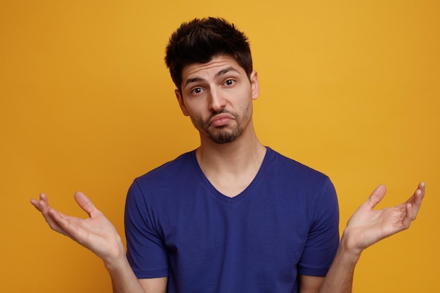 Confused young handsome man looking at camera showing empty hands on yellow background