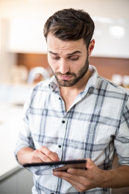 Confused young man using digital tablet in kitchen
