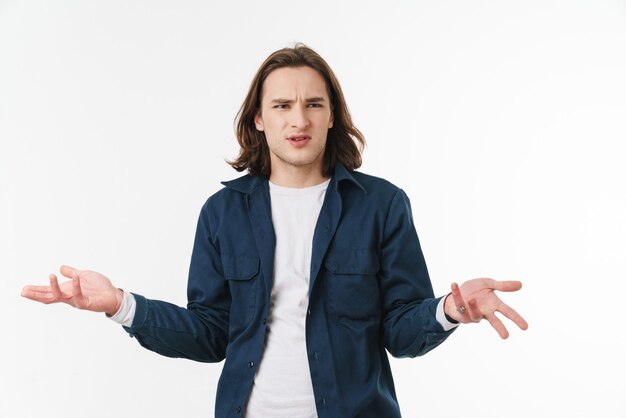 confused young man with long hair posing and throwing up hands isolated over white wall