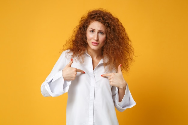 Confused young redhead woman girl in casual white shirt posing isolated on yellow orange wall