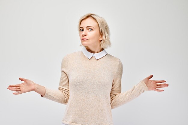 Confused young woman shrugging her shoulders on a white background