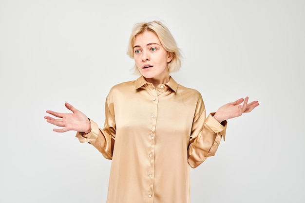 Confused young woman in a silk blouse shrugging her shoulders isolated on a white background