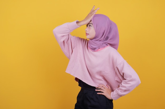 Confused of young woman with holding her head, wearing yellow wall