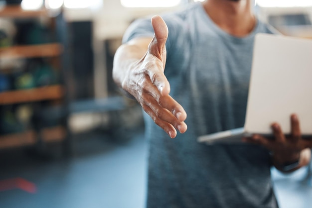 Congrats on signing up with us Closeup shot of an unrecognisable man extending a handshake while using a laptop in a gym