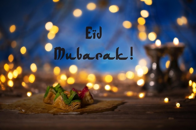 Congratulation eid mubarak arabic sweets on a wooden surface\
candle holders night light and night blue sky with crescent moon in\
the background