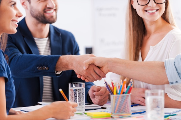 Congratulations! Close-up of business people in smart casual wear shaking hands and smiling while sitting at the table together