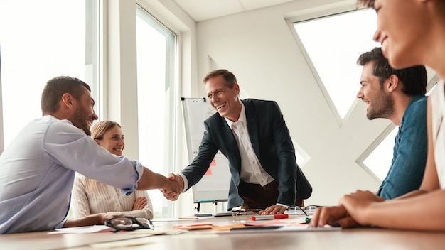 Congratulations Two cheerful colleagues shaking hands and smiling while sitting in the modern office. Teamwork. Meeting