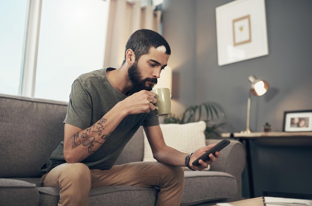 기술의 용이함으로 현재의 모든 것에 연결 집에서 소파에서 커피를 마시고 스마트폰을 사용하는 젊은 남자의 샷