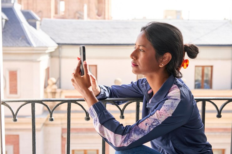 Photo connected and entertained young indian woman enjoys her phone while sitting on the windowsill