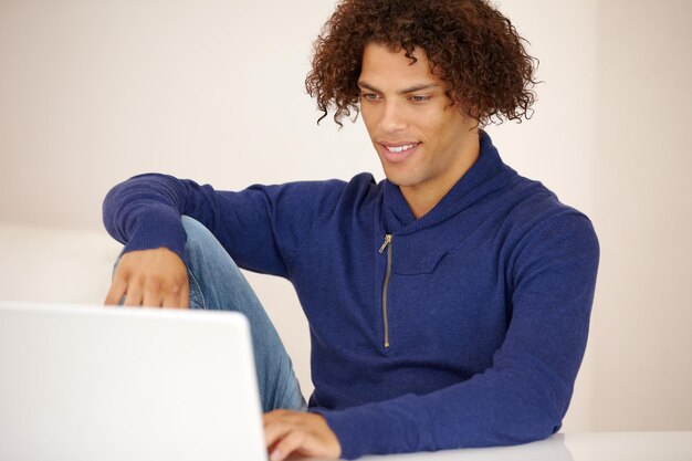 Connecting from the comfort of my couch Handsome young ethnic man working on his laptop on his couch