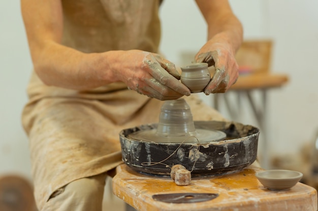 Connecting pieces. Man with dirty hands wearing protective apron while working and holding wet tiny plate