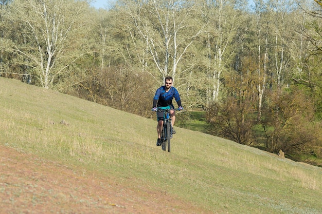 Покорение горных вершин велосипедистом в шортах и майке на современном карбоновом хардтейле с вилкой на пневматической подвеске
