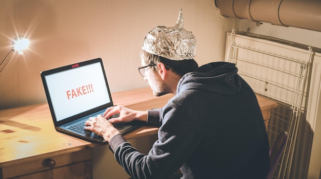 Conspiracy theory concept jonge man met aluminium dop die op internet zoekt terwijl hij eenzaam in de donkere kelder zit