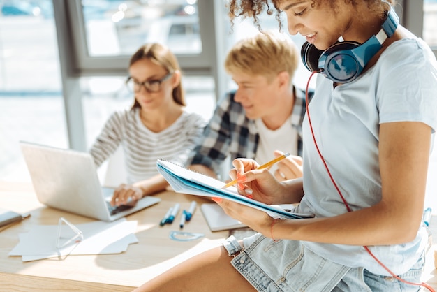 Costante educazione. piacevole giovane donna afro americana sorridente che prende appunti mentre era seduto sul tavolo e studiava con i suoi compagni di gruppo