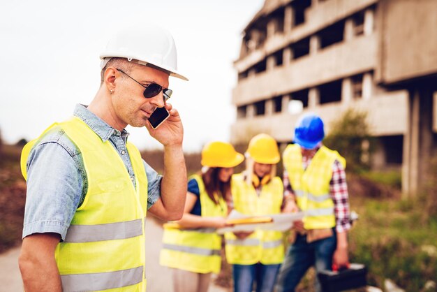 Construction architect using phone in front building damaged in the disaster. Selective focus, focus on architect.