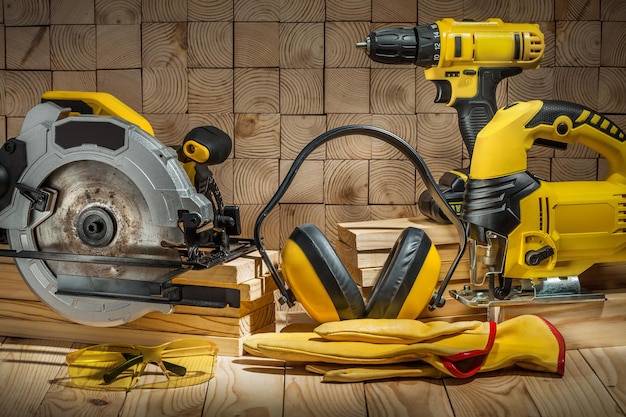 Construction carpentry tools electric corded circular saw\
jigsaw cordless drill earphones gloves goggles on wooden\
background