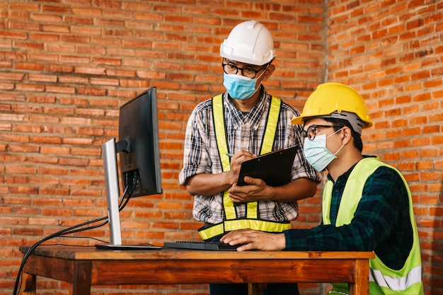 Construction concept of Engineer and Architect are to wear medical masks working at Construction Site Via monitor for review due to the global impact of COVID-19 and Social Distancing.