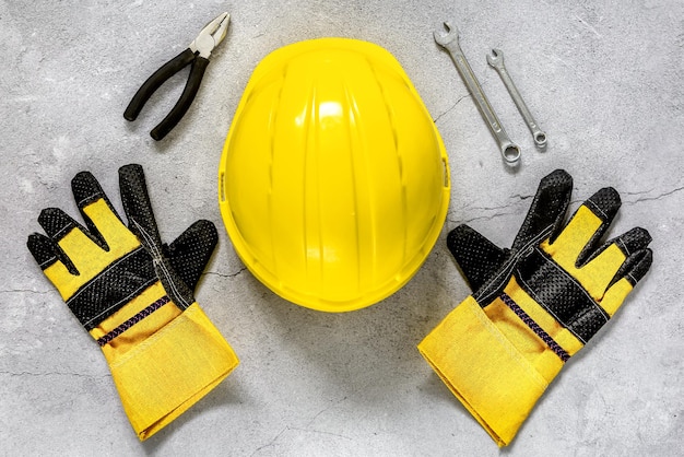 Construction concept yellow protective helmet and gloves on a gray concrete background top view