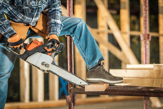 Photo construction contractor cutting wood board using powerful chainsaw power tool wooden skeleton structure of residential building construction industry theme