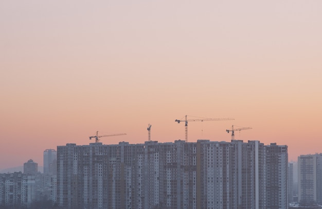 Construction cranes by the constructing building in the city at sunrise or sunset