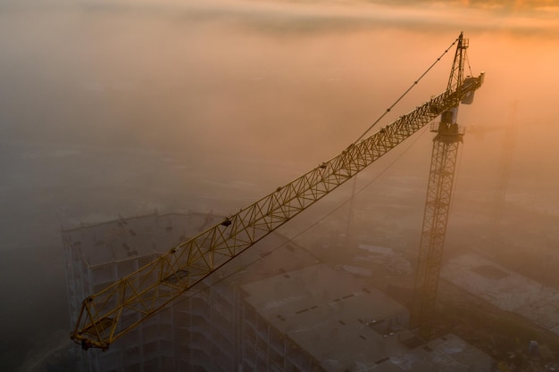 Construction cranes at dawn in the morning mist.