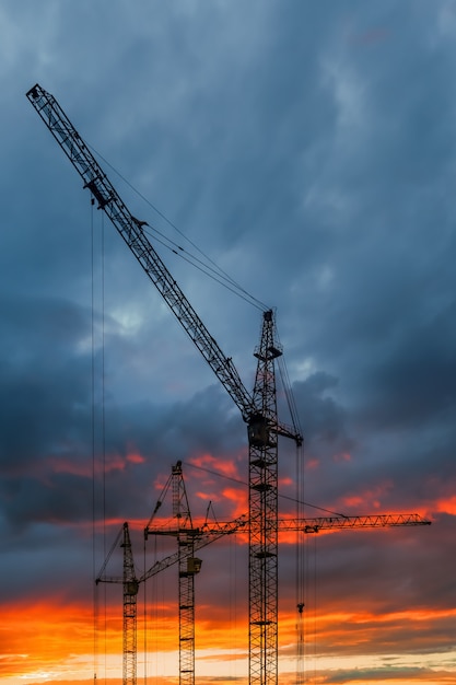 Construction cranes silhouette against sunset sky