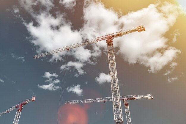 Construction cranes work on creation site against blue sky background. Bottom view of industrial crane. Concept of construction of apartment buildings and renovation of housing. Copy space