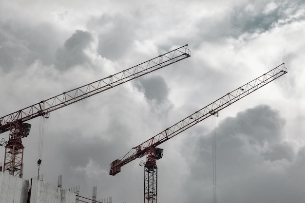 Construction cranes work on creation site against blue sky background Bottom view of industrial crane Concept of construction of apartment buildings and renovation of housing Copy space