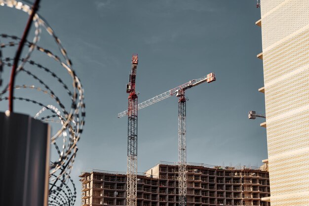 Construction cranes work on creation site against sky background