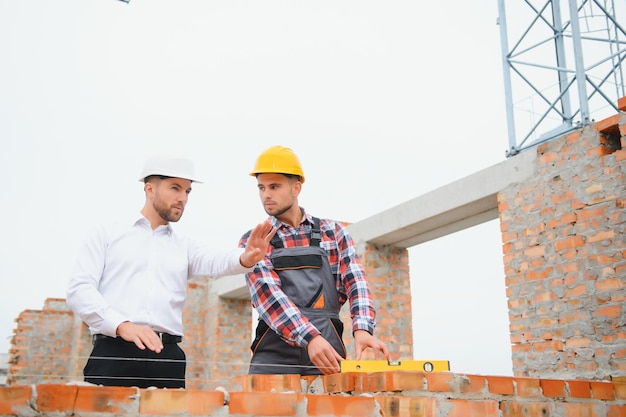 Construction engineers supervising progress of construction project stand on new concrete floor top roof and crane background