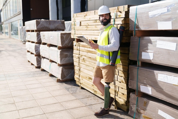 写真 安全ベストを着た建設専門家が積み重ねられたパレットのそばで品質管理のための材料を評価しています