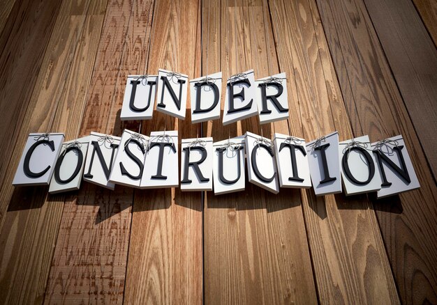 Under Construction hanging from strings against a wooden planks background