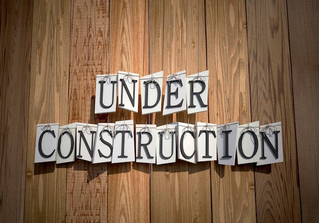 Under Construction hanging from strings against a wooden planks background