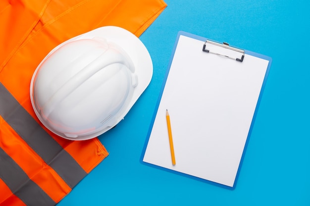 construction hard hat with safety vest isolated on blue with clipboard