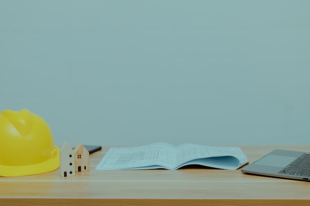 Construction helmet, a little wood house, a book and a notebook on a desk