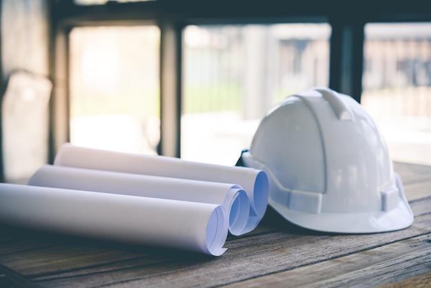 建設家。修理作業。建物のための図面と木製テーブル上のヘルメット。