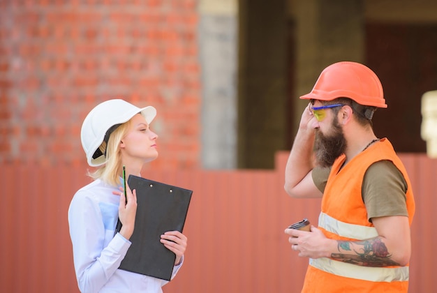 Concetto di industria edile relazioni cliente edile e partecipante industria edile discutere il piano di avanzamento l'ingegnere donna e il costruttore brutale barbuto discutono dei progressi della costruzione