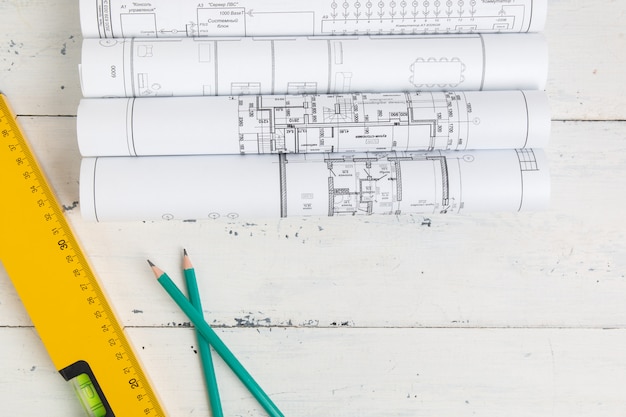 Construction level, drawings, blueprints and pencils on a white table