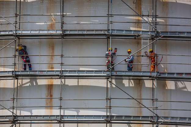 Construction male workers tank oil installing scaffolding on site refinery