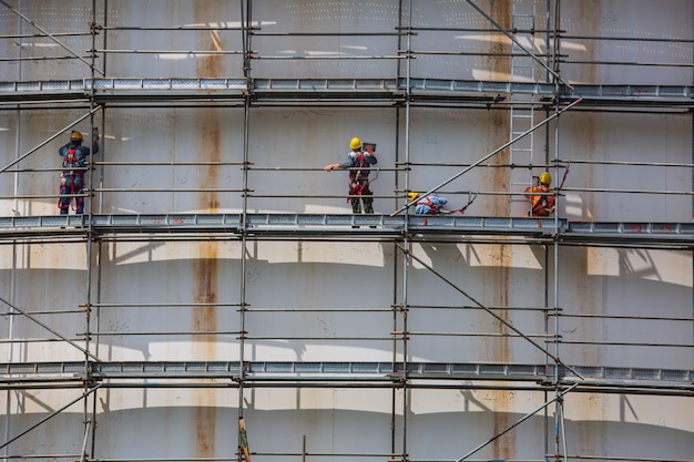 Construction male workers tank oil installing scaffolding on site refinery