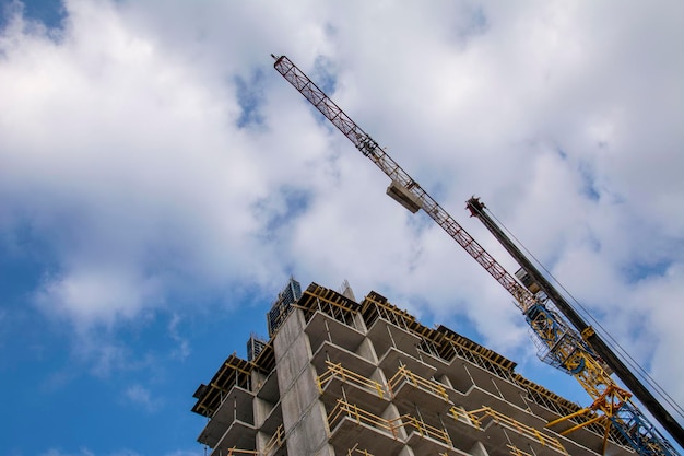 多階建ての住宅の建設。青い空と雲を背景にした鶴と未完成の建物。