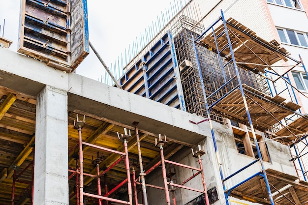 Construction of a new monolithic reinforced concrete house\
scaffolding on the facade of a building under construction working\
at height on a construction site