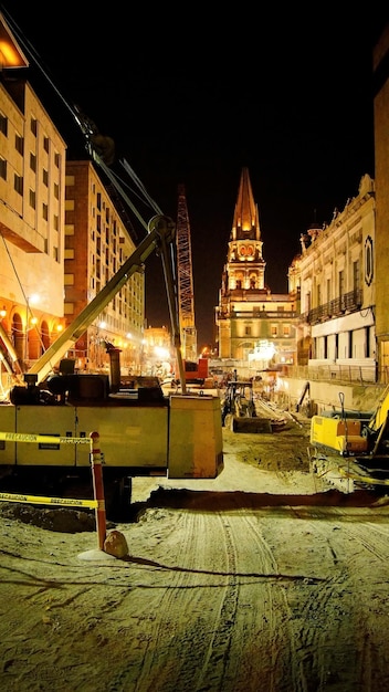 Construction at night heavy machinery backhoe grader road roller a church in the background