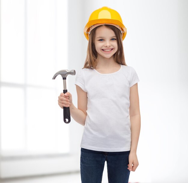 construction and people concept - smiling little girl in protective helmet with hammer