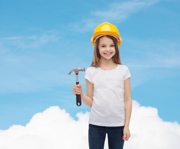 construction and people concept - smiling little girl in protective helmet with hammer