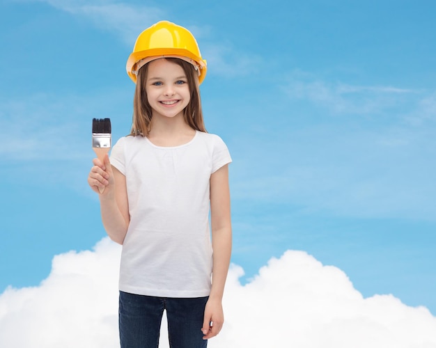 construction and people concept - smiling little girl in protective helmet with paint brush