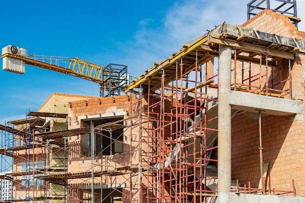 Construction of a red brick multi-storey building. The use of scaffolding when building a house. Industrial and civil construction. Construction safety.